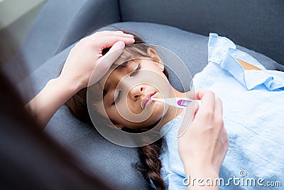 Mother hand taking temperature with girl is a sick laying on sofa, Kid patient with mom check thermometer Stock Photo