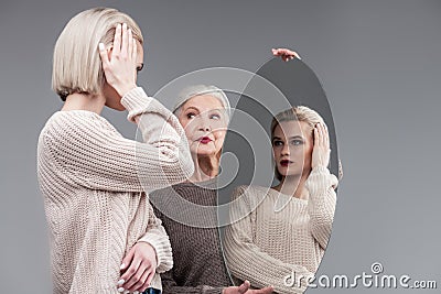 Attentive blonde woman refreshing her bob haircut in round mirror Stock Photo