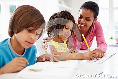 Mother Helping Children With Homework In Kitchen Stock Photo