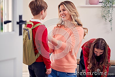 Mother Helping Children In Uniform To Get Ready To Leave Home For School Stock Photo