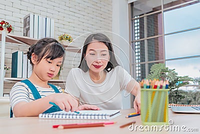 Mother helping her daughter doing creative art homework coloring pencil book at home for family togetherness concept Stock Photo