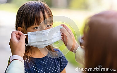 Mother helping her daughter to wear medical face mask Stock Photo