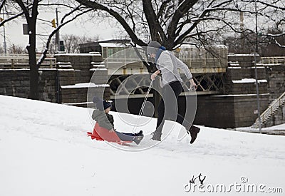 Mother helps her child ride sleigh in snow in Bronx NY park Editorial Stock Photo