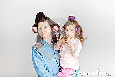 Mother and her child daughter with a lipstick. Portrait of a lovely little baby girl and her mum with curlers on their heads Stock Photo