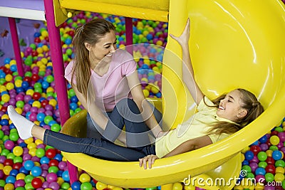 Mother and her daughter having good time on slide at kids playground, indoors Stock Photo