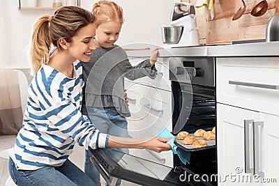 Mother and her daughter taking out cookies from oven Stock Photo