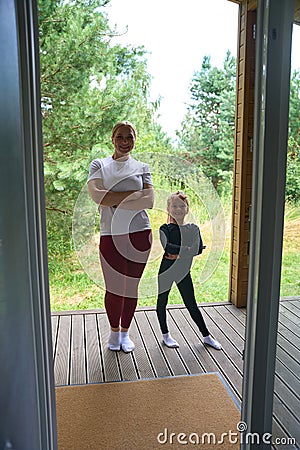 Mother and her little daughter folding hands on chest standing on spacious porch Stock Photo