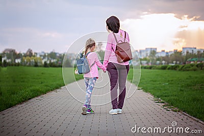 Mother and her little dauther with backpack walking in summer day. View from a back. Stock Photo