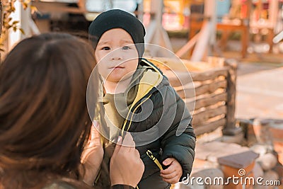 Mother with her little asian son in autumn park copy space. Woman zips up child jacket. Fall and motherhood concept Stock Photo