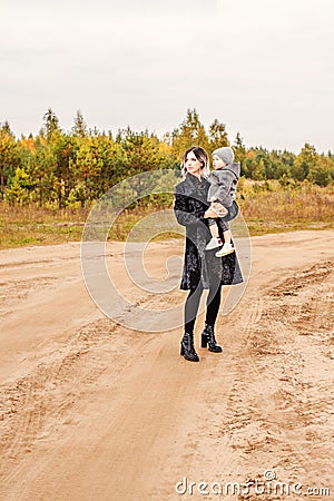 Mother with her son in her arms are going down the dusty sandy rural road Stock Photo