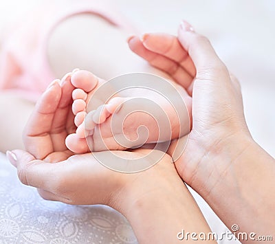 Mother holding baby feet. Closeup of tiny newborn baby feet held by a parent. Small baby toes. Little baby lying on a Stock Photo