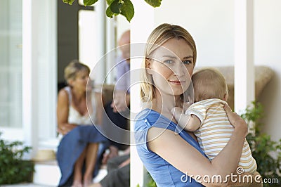 Mother Holding Baby On Porch With Grandparents Behind Stock Photo