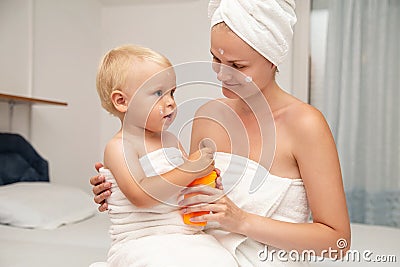 Mother and infant baby in white towels after bathing apply sun screen or after sun lotion or cream. Children skin care. Spf, skin Stock Photo
