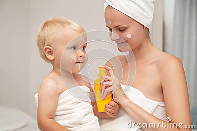 Mother and infant baby in white towels after bathing apply sunscreen or after sun lotion or cream. Children skin care in a hotel Stock Photo