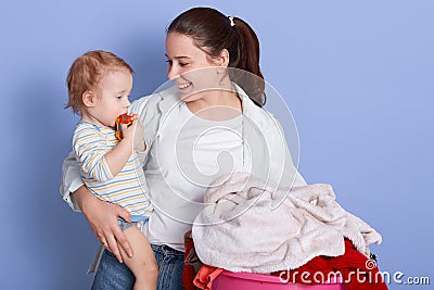 Mother with infant son sitting near laundry basin, mummy looking at her baby with love, cheeper wearing stripped bodysuit nibbles Stock Photo