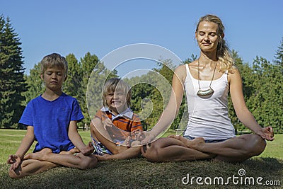 Mother with kids meditating on green grass Stock Photo