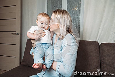 Mother kisses baby and hugs. the concept of happy motherhood. mother and child sitting on sofa at home Stock Photo