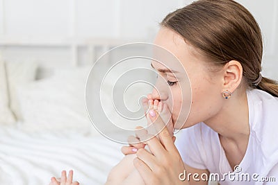 Mother kisses baby`s feet and sniffs them on the bed at home, happy motherhood Stock Photo