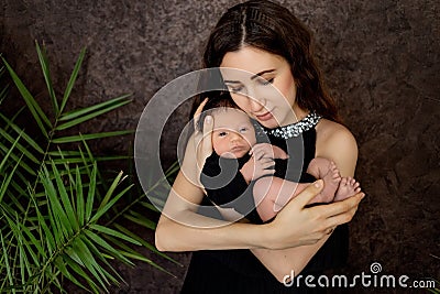 Mother lies on the bed with a newborn baby on a dark background, hugs her son 7 days, family day, mother`s love and care Stock Photo