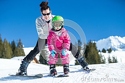 Mother and little child skiing in Alps mountains. Active mom and toddler kid with safety helmet, goggles and poles. Stock Photo