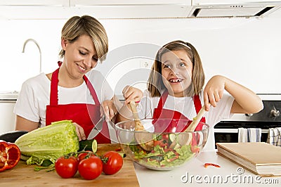 Mother and little daughter cooking together with cook apron preparing salad at home kitchen Stock Photo