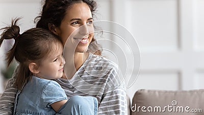 Mother and little daughter sit on sofa smiling looking away Stock Photo