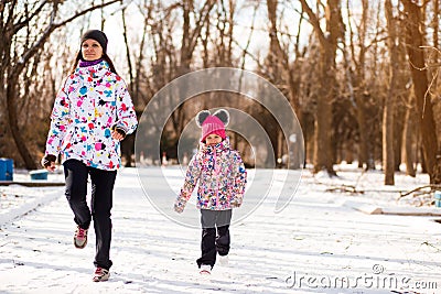 Mother and little girl in colored jackets jogging by snow in winter park. Concept of instill sports health habits Stock Photo