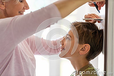 Mother measuring the height of her son against wall Stock Photo