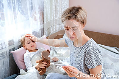Mother measuring temperature of her ill child. Sick child with high fever laying in bed with teddybear. Fever Concept Stock Photo