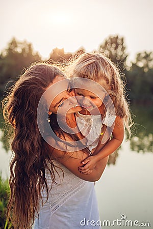 Mother playing and having fun with daughter by summer river at sunset. Woman holding kid and laughing. Family Stock Photo