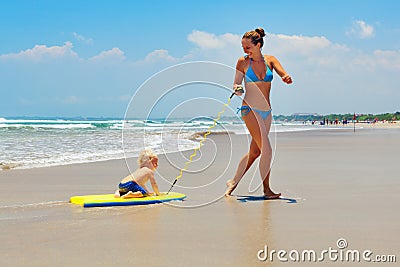 Mother pull baby son on surfing board by sea beach Stock Photo