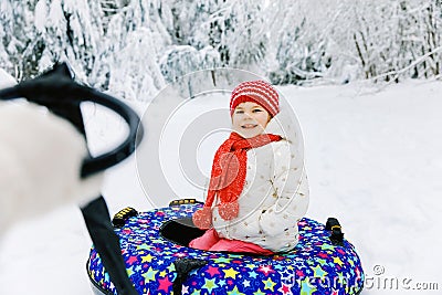 Mother pull little toddler girl on snow tube. Cute little happy child having fun outdoors in winter on colorful tire Stock Photo