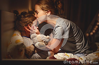 Mother puts her daughter to bed and kisses her in evening Stock Photo