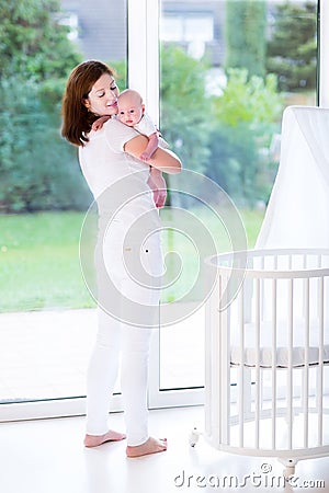 Mother putting newborn baby in bed next to window Stock Photo