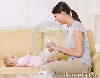 Mother putting shoes on baby on sofa at home Stock Photo