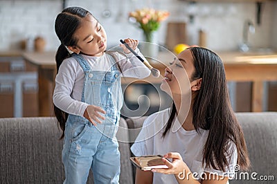 Caring child applying the compact powder to her female parent Stock Photo