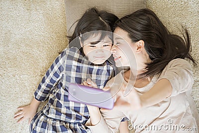Mother is selfie with her little daughter using a smart phone camera while kissing daughter cheek. Stock Photo