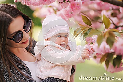 Mother show firs time to her daughter pink tree. Happy baby hold branch of sakura Stock Photo