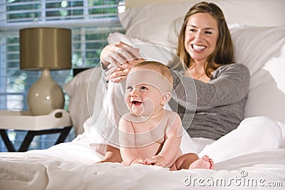 Mother sitting on bed with amused baby Stock Photo