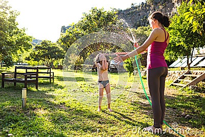 Mother sprays a child with a hose in the courtyard of the house, Boy drenched in water on a hot sunny day Stock Photo