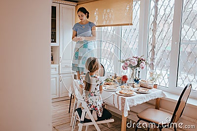 Mother is standing on the stool and making photo of the kitchen table with different courses for the breakfast and her Stock Photo