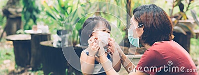 Mother take care daughter with face mask for protection disease flu or covid-19 outdoors. Stock Photo