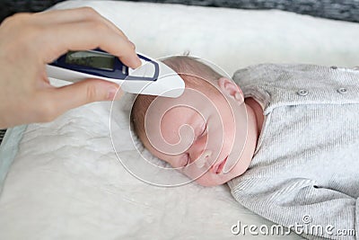 Mother takes temperature for her newborn with infrared thermometer at home Stock Photo