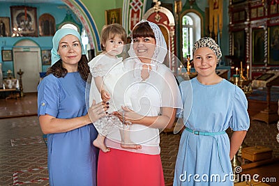 Mother with toddler and teenage daughters standing in the Orthodox church, godmother holding her goddaughter in arms Stock Photo