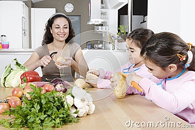 Mother and Twins Peeling Potatoes in Kitchen Stock Photo