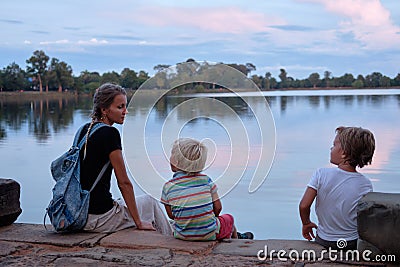 Mother and two sweating tired sons rest evening sunset near lake. Angkor Wat, Cambodia Stock Photo