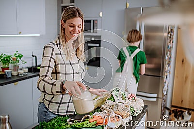 Mother unpacking local food in zero waste packaging from bag in kitchen at home. Stock Photo