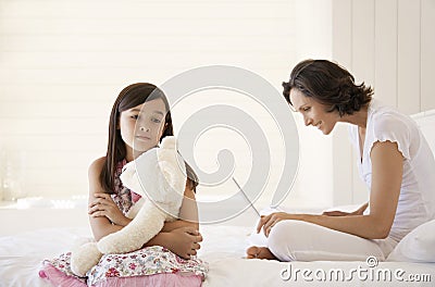 Mother Using Laptop With Daughter Holding Teddy Sitting On Bed Stock Photo