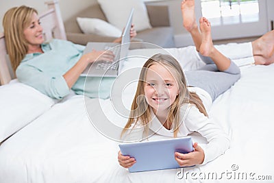 Mother using laptop while daughter using tablet pc on the bed Stock Photo