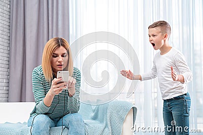 Mother using mobile phone while her son screaming and asking for attention. Lonely despaired child Stock Photo